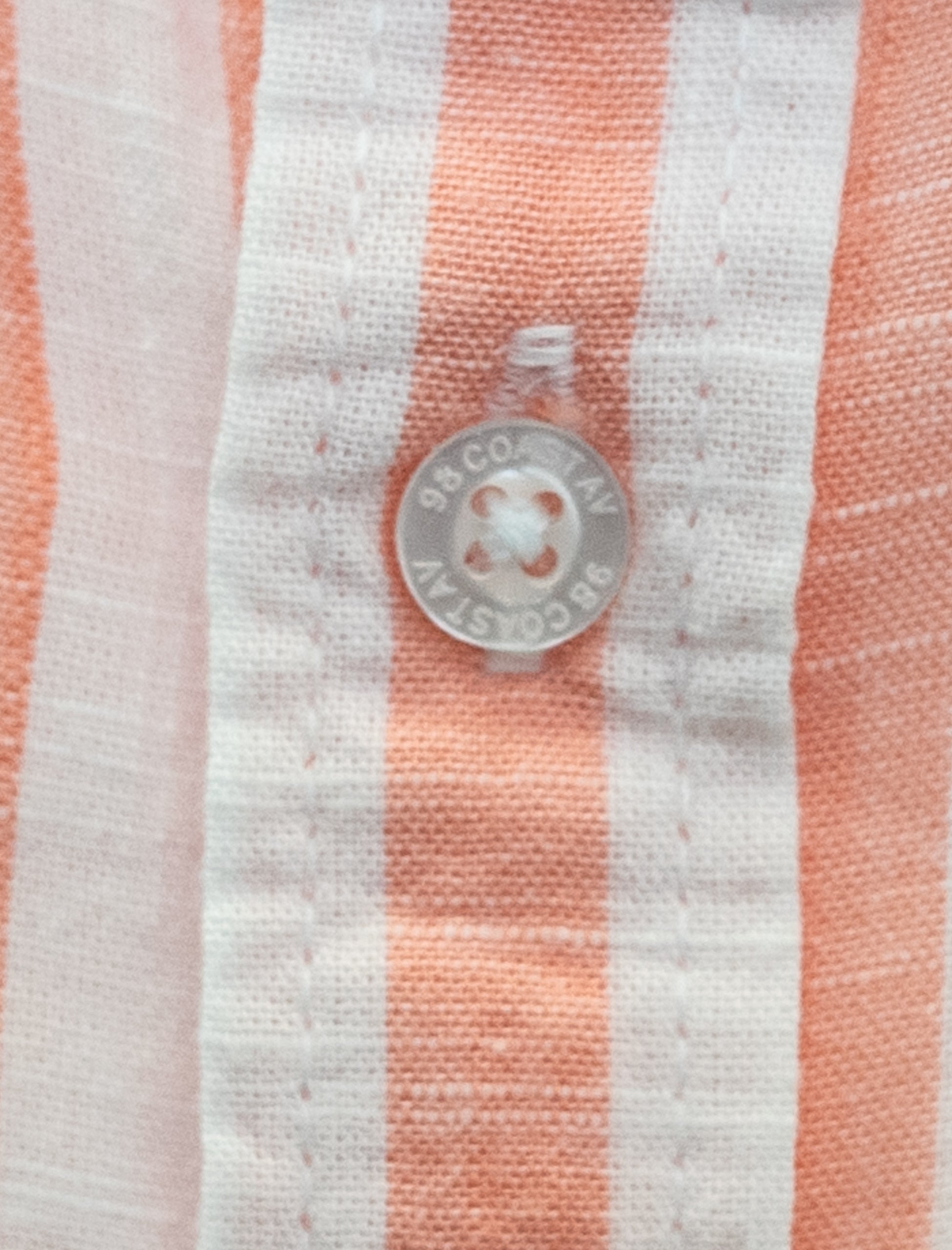 Detalle de la textura y botón en camisa rayada durazno para niño