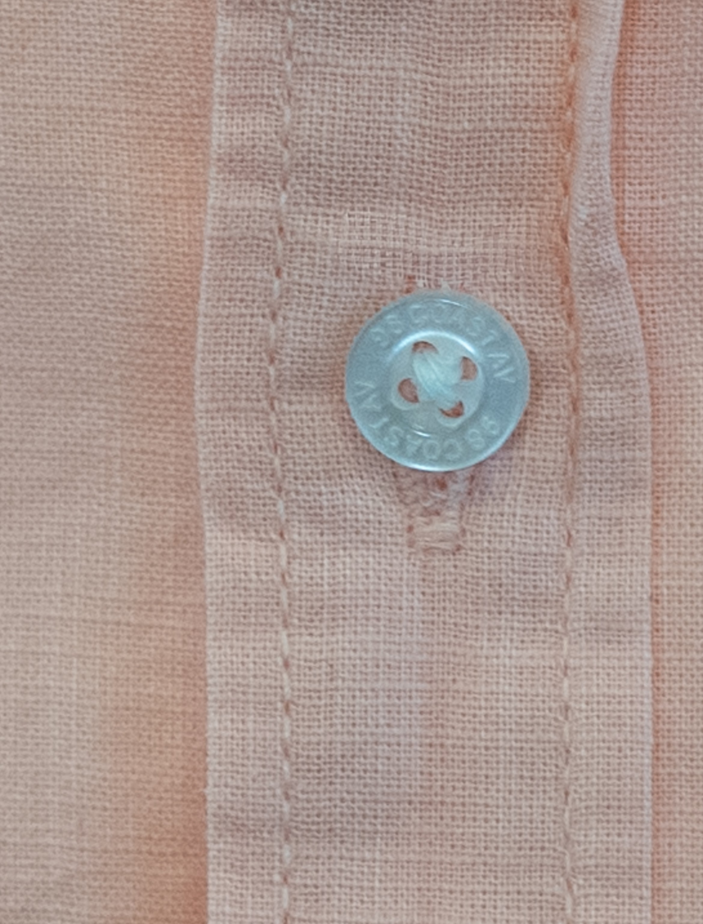 Detalle de textura y botón en camisa infantil de algodón slub color durazno