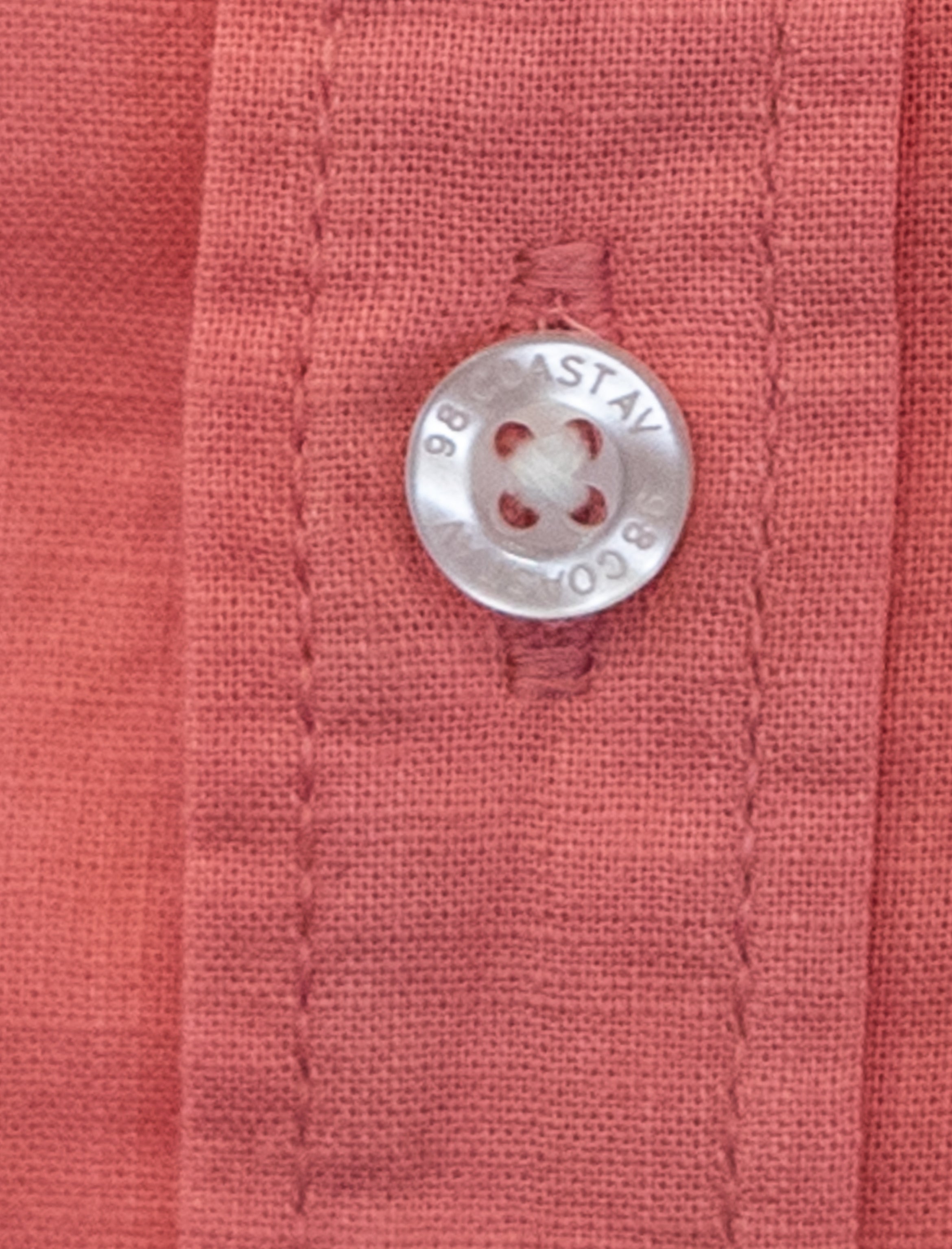 Detalle de textura y botón en camisa infantil de algodón slub color rosa